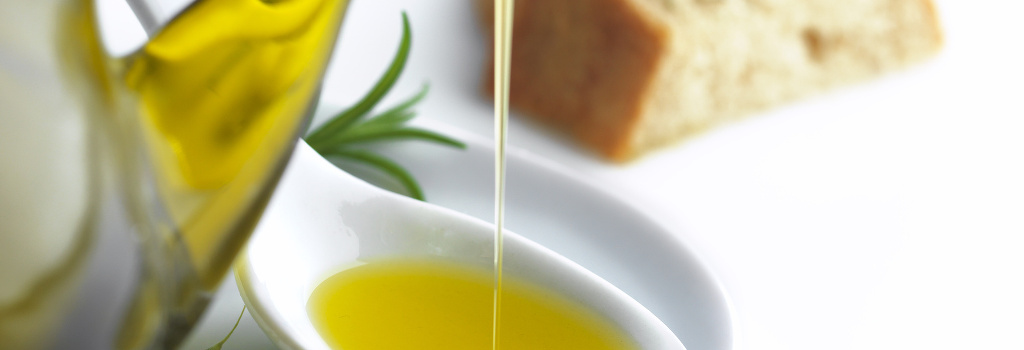 pouring olive oil on a spoon and a slice of bread with oregano